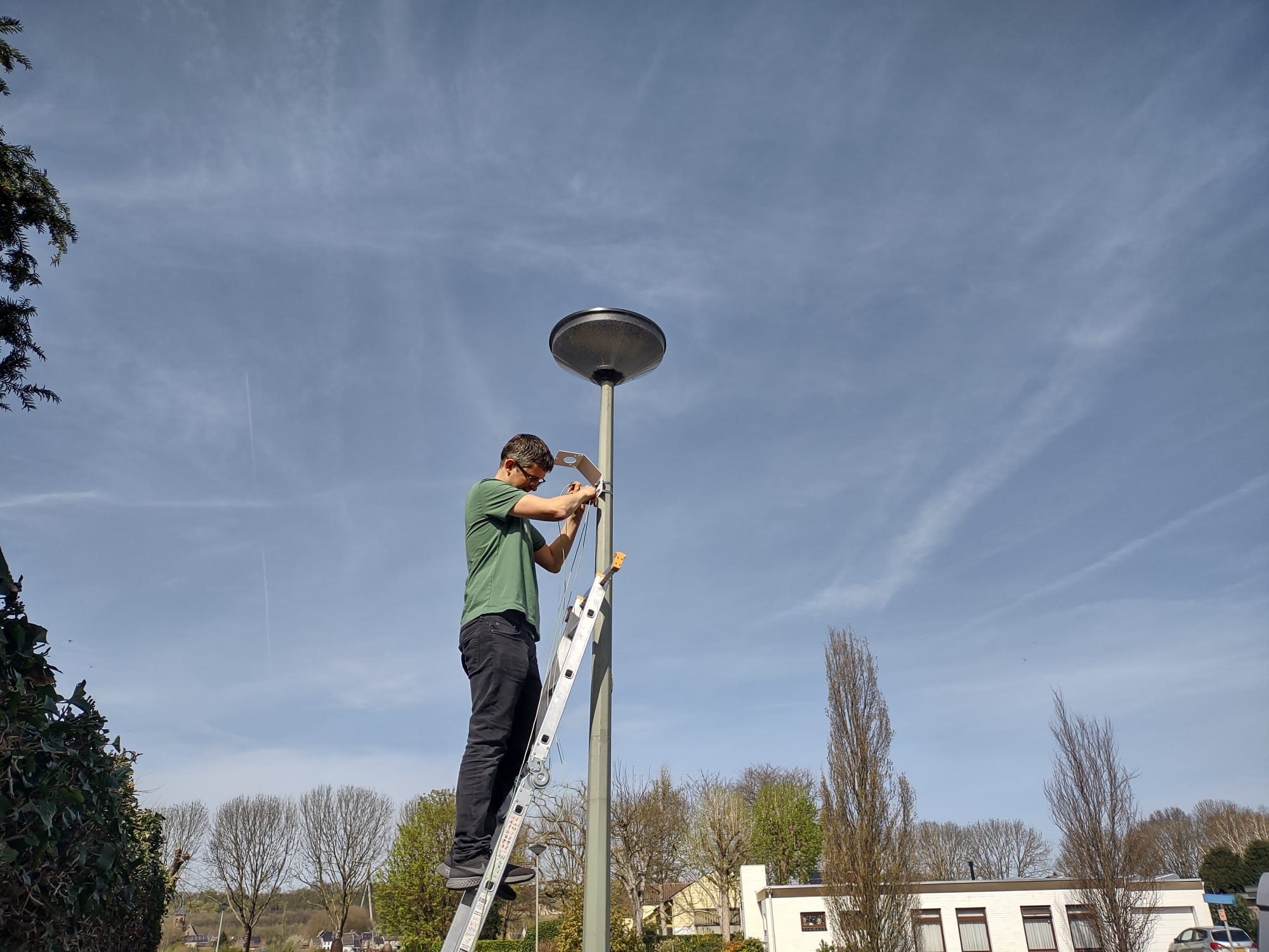 Man op ladder installeert meetapparatuur luchtkwaliteit aan lantaarnpaal. 